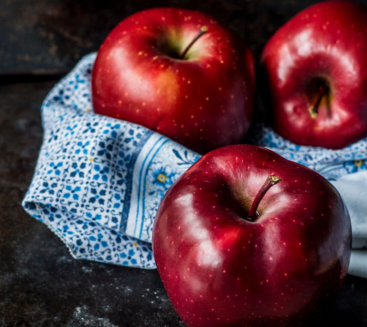 Drei rote glänzende Äpfel auf einem blauen Küchentuch